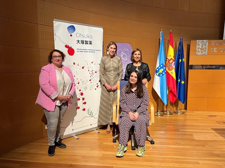 Nuria Carballeda, presidenta de la Asociación Galega de Lupus; Natalia Lobato, Secretaria General Técnica de la Consellería de Sanidade de la Xunta de Galicia; Montse Sánchez-Agustino, Regional Market Access Manager de Otsuka Pharmaceutical y sentada, Miriam Fernández, la conferenciante.